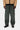 Pantalon Carhartt WIP Single Knee vert foncé porté par un homme avec une veste beige et un pull noir.