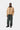 Homme portant le Pantalon Single Knee Carhartt WIP vert foncé, une veste beige, un pull gris et des chaussures marron.