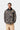Homme portant une veste Carhartt WIP Lander Coat camouflage avec col en velours côtelé noir et pantalon beige sur fond uni.