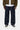 Pantalon Aaron Carhartt WIP bleu foncé, coupe ample, porté avec une chemise blanche, une veste kaki et des baskets noires.
