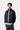 Veste Bolon Dark Navy Carhartt WIP bleue marine, à logo blanc, portée par un homme avec une chemise rayée. Vue de face sur fond blanc.