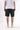 Back view of a person wearing black Classic Chef Shorts by Service Works and a white t-shirt. An orange label is visible on the shorts.