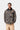Homme portant une veste Carhartt WIP Lander Coat camouflage avec col en velours côtelé noir et pantalon beige sur fond uni.