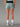 Vue arrière du Short Trail LEVICO AYAQ vert sauge avec taille noire, porté par une femme en tenue de sport.